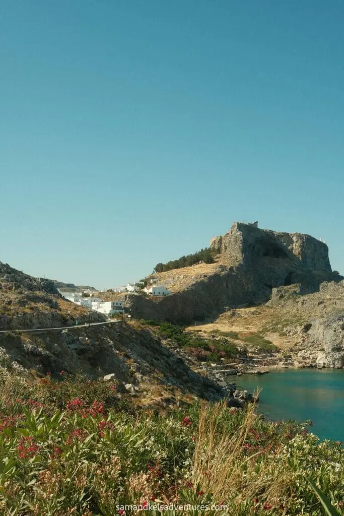 traveling to greece tips view of castle and acropolis with plants in the foreground and white buildings